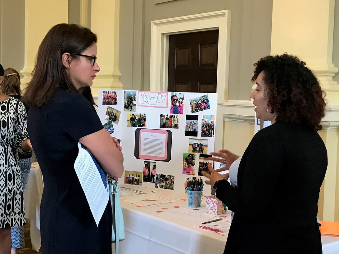 A woman at a nonprofit exhibition explains a display board of photographs to another attendee, showcasing storytelling through images.